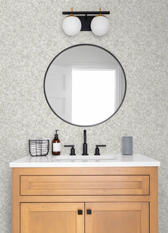 Modern bathroom vanity with light wood cabinet, round mirror, matte black faucet, soap dispenser, wire basket, and gray smart speaker on a white countertop set against York Wallcoverings’ Hepworth Texture Wallpaper. Light fixture above mirror.