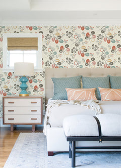 Bright bedroom featuring the Jonah Leaf Trail Wallpaper by York Wallcoverings, a bed adorned with blue and peach pillows and a beige tufted headboard, a light wood nightstand topped with a turquoise lamp, and a cushioned bench at the foot of the bed.