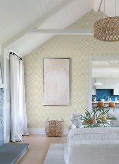 Sure! Here’s a rewritten version of your sentence incorporating the product data: Bright living room with vaulted ceiling, York Wallcoverings’ Lars Retro Wave Wallpaper, abstract art, woven basket, light sofa, and view into a kitchen with blue backsplash and two wooden stools at an island.