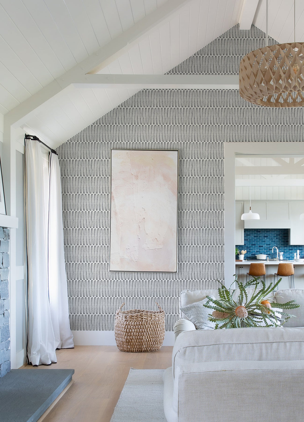 Bright living room featuring the Lars Retro Wave Wallpaper by York Wallcoverings, abstract art, a woven basket, white sofa, green plant, and a view into a modern kitchen with blue backsplash and wooden barstools.
