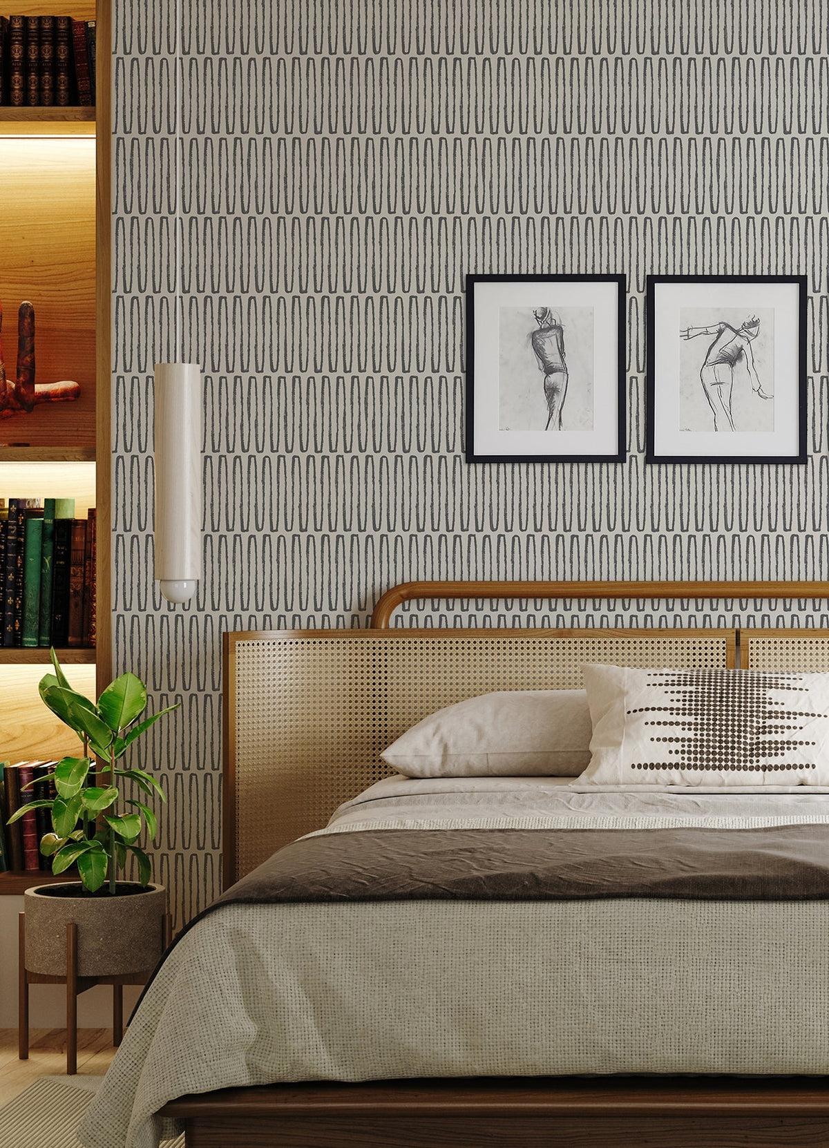 A modern bedroom featuring York Wallcoverings’ Lars Retro Wave Wallpaper, two framed sketches displayed above a cane headboard, neutral bedding accented with a decorative pillow, a potted plant, and built-in shelves styled with books and art objects.