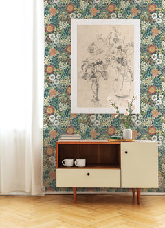A mid-century cabinet with two cups sits by a wall covered in York Wallcoverings’ Karina Wildflower Garden Wallpaper, which features a large line-drawing of flowers in a vase. Natural light streams in from a white curtain on the left.