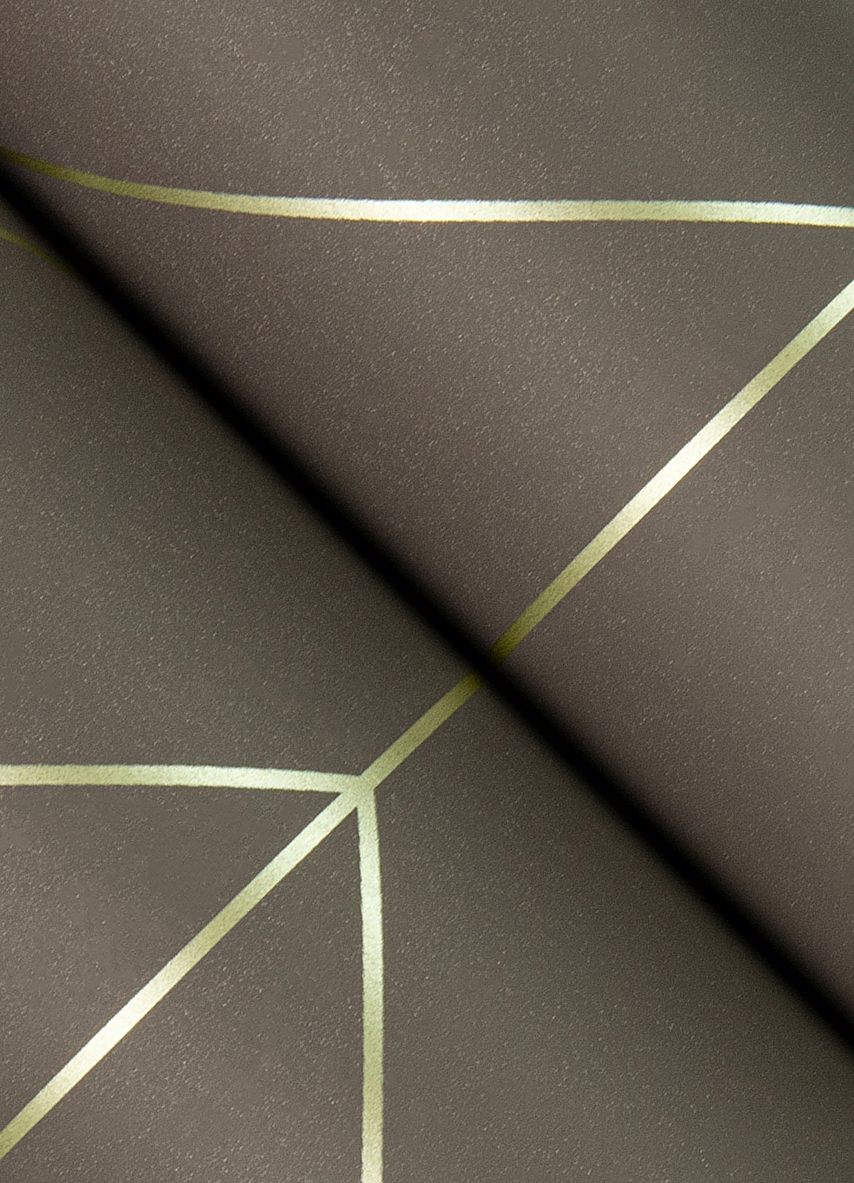 A close-up of York Wallcoverings’ Sander Geometric Wallpaper, featuring a textured dark surface with thin metallic gold lines that intersect to form abstract geometric patterns.