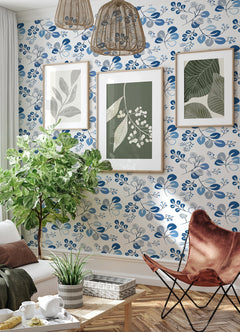 Sure! Here’s your sentence rewritten to include the provided product data: Cozy living room featuring Jonah Leaf Trail Wallpaper by York Wallcoverings, a lush green leafy plant, three botanical prints on the wall, a brown butterfly chair, a white sofa, and woven rattan pendant lights.