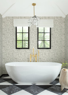 Modern bathroom with a white oval bathtub, gold faucet, geometric pendant light, two windows, black-and-white checkered floor tiles, and York Wallcoverings Chesapeake Plumeria Floral Trail Wallpaper.