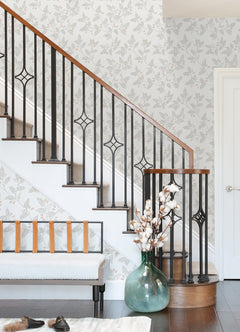 A staircase with dark railings and wooden handrail, Ardell Botanical Wallpaper by York Wallcoverings, a bench featuring a leather strap backrest, and a large green vase filled with cotton branches on a dark wood floor.