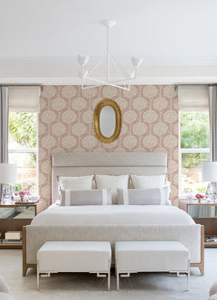 Contemporary bedroom featuring a large bed, two windows, a gold oval mirror above the headboard, white benches at the foot of the bed, a modern ceiling light fixture, and Zaria Topiary Wallpaper by York Wallcoverings.