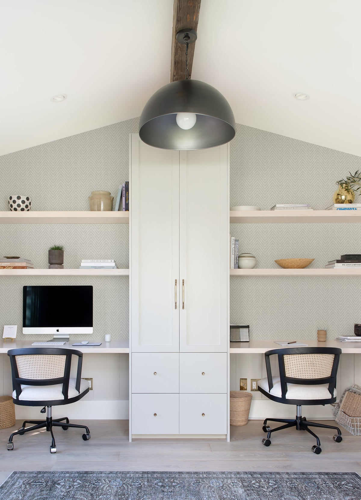 Sure! Here’s a rewritten sentence that incorporates the product data: Modern home office featuring Glynn Chevron Wallpaper by York Wallcoverings, two desks, black chairs, a computer, shelves with décor and books, a central tall cabinet, and a large black light fixture hanging from the ceiling.