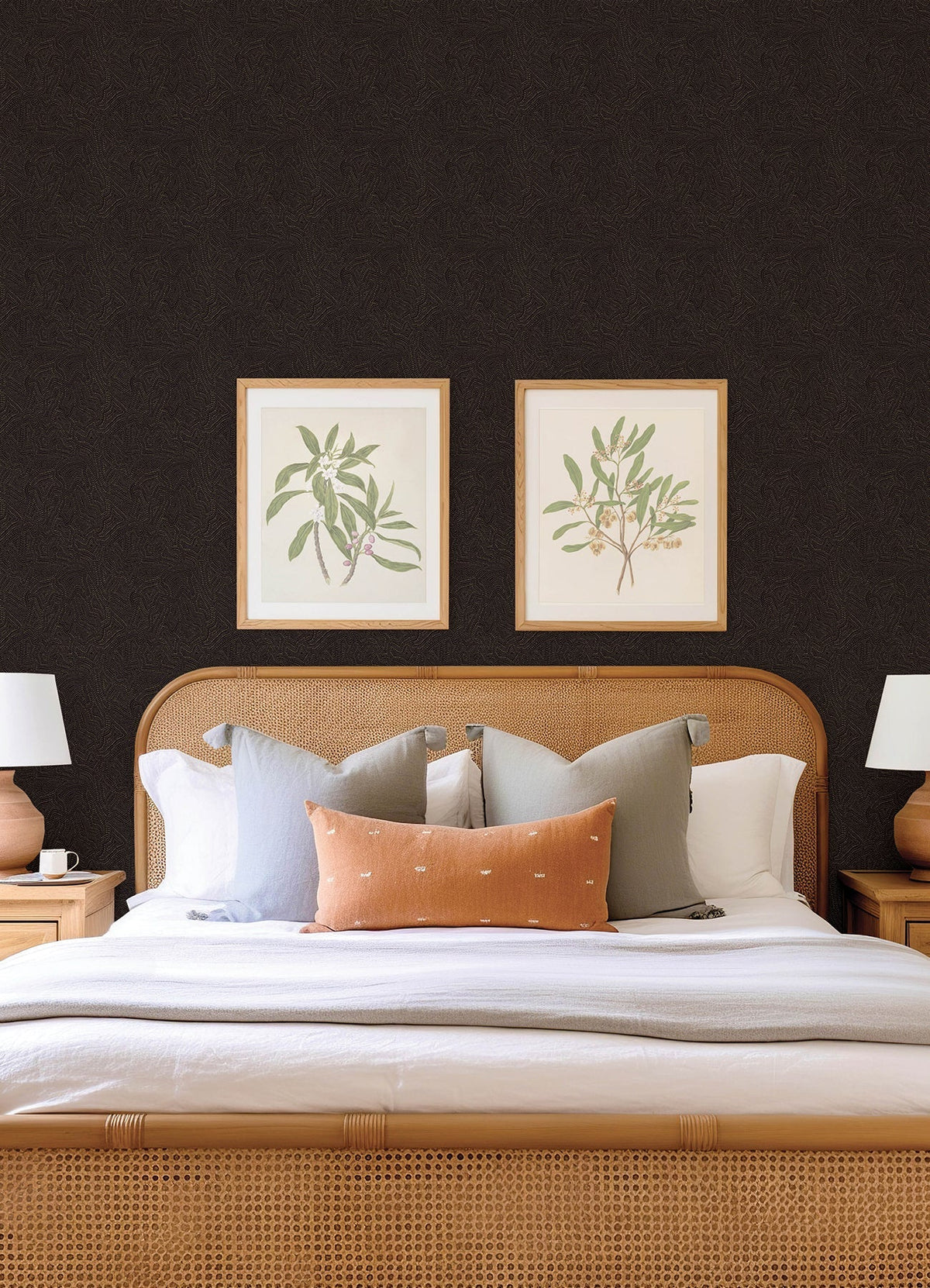 A neatly made bed with multiple pillows, flanked by two wooden nightstands and white lamps, sits against a wall adorned with Hollenback Dotted Abstract Wallpaper by York Wallcoverings, with two framed botanical prints displayed above the headboard.