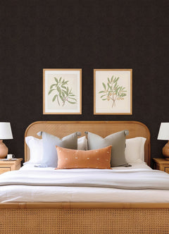 A neatly made bed with multiple pillows, flanked by two wooden nightstands and white lamps, sits against a wall adorned with Hollenback Dotted Abstract Wallpaper by York Wallcoverings, with two framed botanical prints displayed above the headboard.
