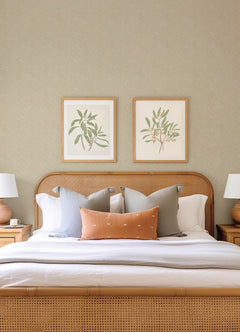 A neatly made bed with neutral bedding, decorative pillows, and a cane headboard sits between two wooden nightstands topped with lamps. The wall above the bed features York Wallcoverings’ Hollenback Dotted Abstract Wallpaper as an elegant backdrop.