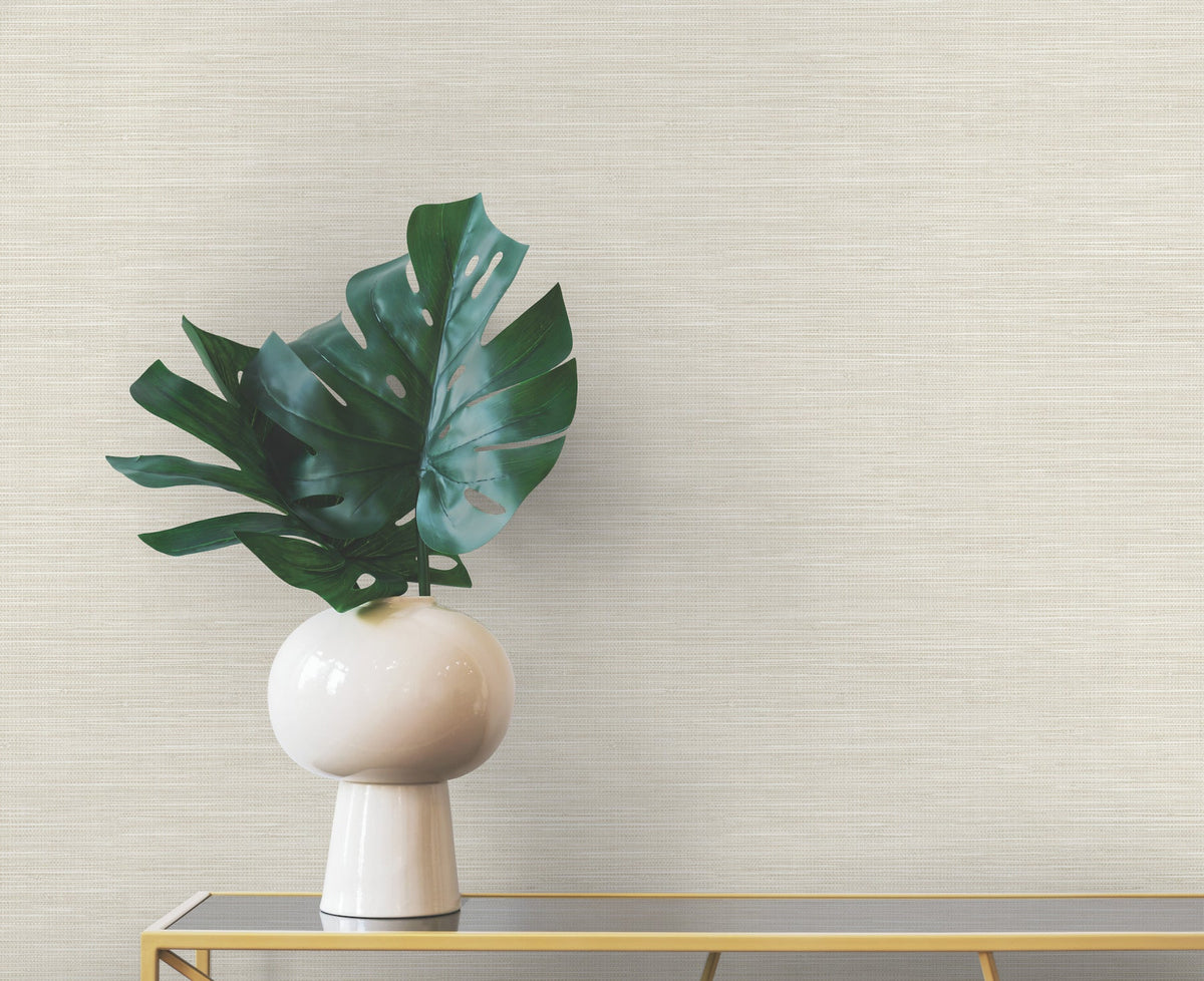A large monstera leaf in a white vase sits on a gold console table against a neutral-colored Winn Faux Grasscloth Wallpaper by York Wallcoverings with a woven texture.