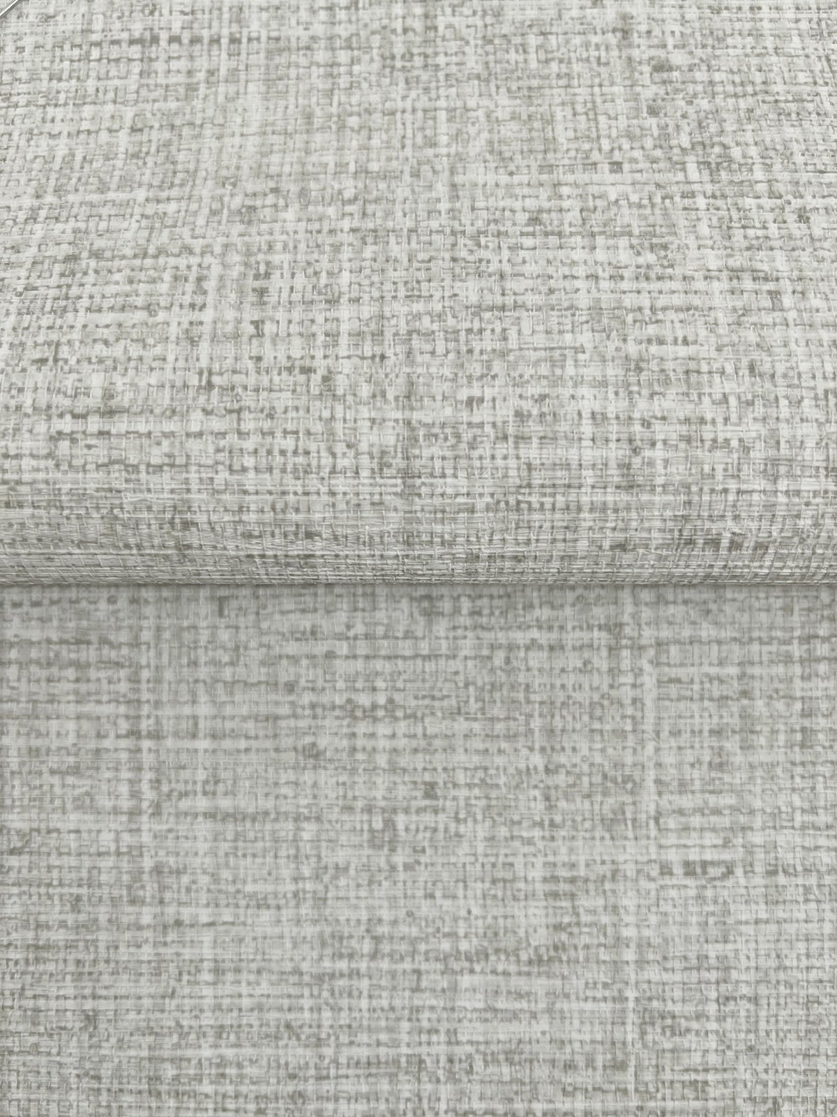 A folded piece of Clarkson Woven Wallpaper featuring a light gray, textured, cross-hatched pattern.