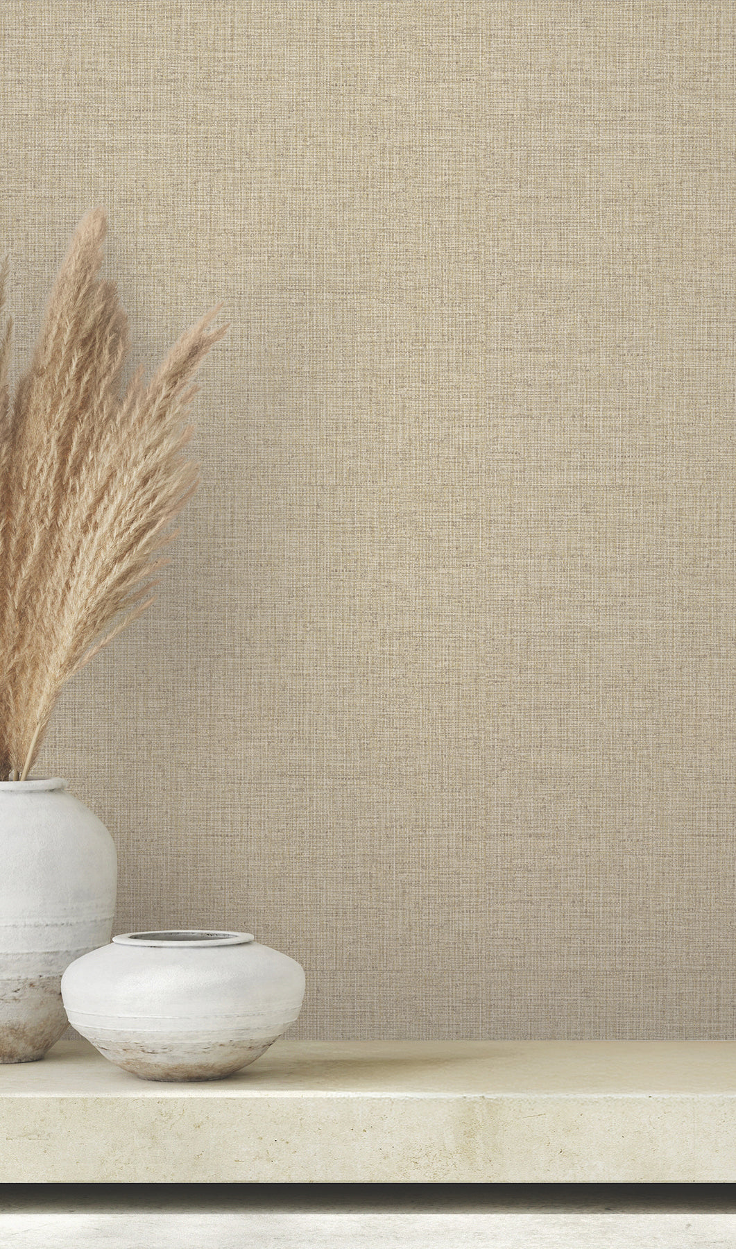 Clarkson Woven Wallpaper in tan with a fine, woven textile texture, shown behind two ceramic vases filled with dried pampas grass.