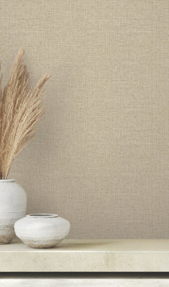 Clarkson Woven Wallpaper in tan with a fine, woven textile texture, shown behind two ceramic vases filled with dried pampas grass.