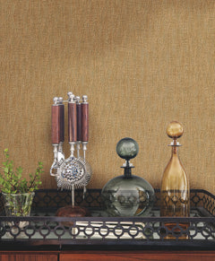 Gold-toned Bryson Feathered Texture Wallpaper with a subtle feathered texture behind a bar cart containing a cocktail tool set and two glass decanters.