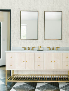 Modern bathroom featuring Chesapeake Ramona Distressed Texture Wallpaper by York Wallcoverings, double sinks with brass faucets, two mirrors, a light wood vanity with brass accents, and black-and-white checkered floor tiles.