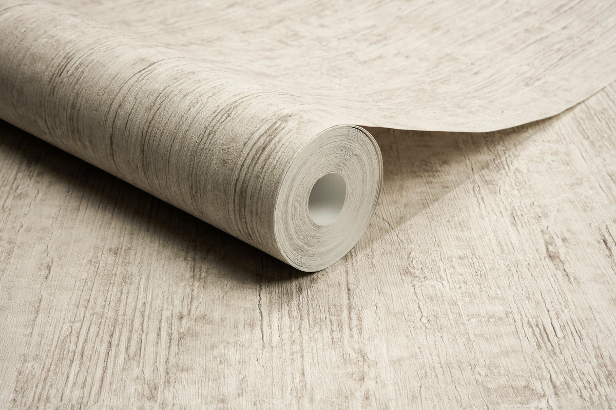 A close-up of a roll of Chesapeake Ramona Distressed Texture Wallpaper by York Wallcoverings, partially unrolled on a matching beige surface.