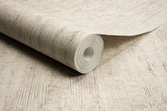 A close-up of a roll of Chesapeake Ramona Distressed Texture Wallpaper by York Wallcoverings, partially unrolled on a matching beige surface.