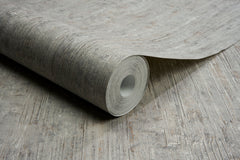 A roll of Chesapeake Ramona Distressed Texture Wallpaper by York Wallcoverings is partially unrolled on a surface featuring a matching wood-like pattern.