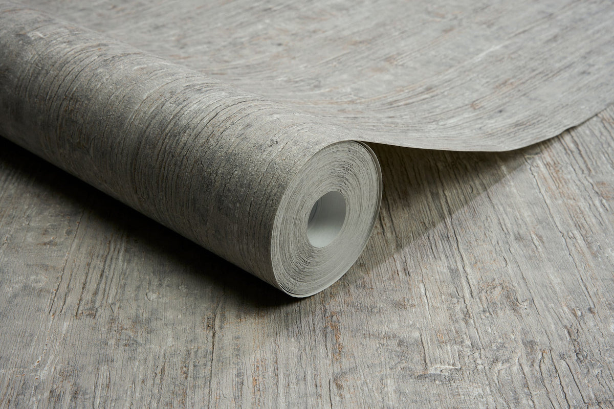 A roll of Chesapeake Ramona Distressed Texture Wallpaper by York Wallcoverings, featuring a textured, wood-like pattern, is partially unrolled on a matching surface.