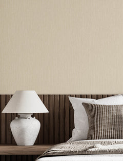 A modern bedroom corner featuring a white ceramic lamp on a wooden nightstand, a brown-striped pillow, and Chesapeake Elijah Texture Wallpaper by York Wallcoverings in the background.