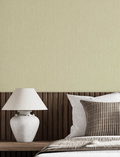 Minimalist bedroom scene featuring a white ceramic lamp on a wooden nightstand, Chesapeake Elijah Texture Wallpaper by York Wallcoverings on the wall, part of a bed with white bedding, and striped brown and white pillows.