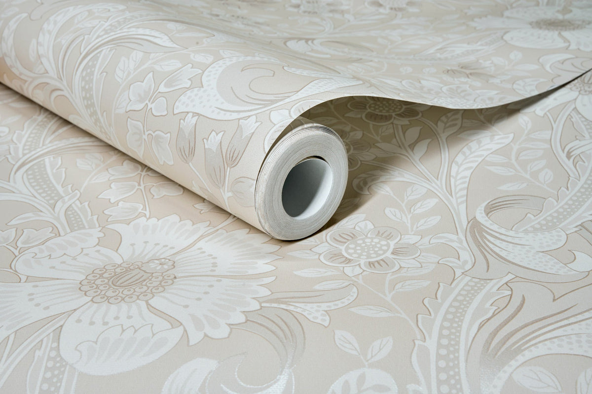 A roll of Chesapeake Liora Floral Trail Wallpaper by York Wallcoverings in light beige, featuring a large, intricate floral pattern, is partially unrolled to display its decorative design on a flat surface.