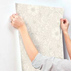 A person in a striped shirt presses Chesapeake Liora Floral Trail Wallpaper by York Wallcoverings onto a white wall, smoothing it out with both hands.