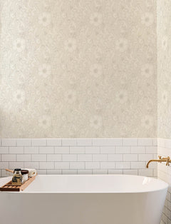 A white bathtub with a gold faucet, white subway tile, Chesapeake Liora Floral Trail Wallpaper by York Wallcoverings, and a wooden tray holding soap and a jar are visible in a bright, modern bathroom.