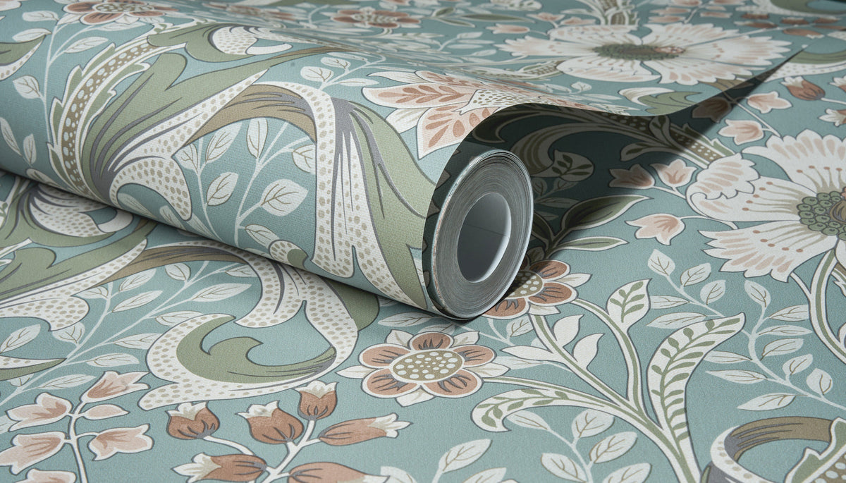 The Chesapeake Liora Floral Trail Wallpaper by York Wallcoverings, featuring a floral and leafy pattern in muted green, blue, cream, and soft pink tones, is shown partially unrolled against a matching background.