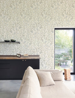 Contemporary living room featuring York Wallcoverings’ Chesapeake Laverne Wildflowers Wallpaper, a beige sofa, black cabinets with a wooden countertop, floating shelves displaying bowls, and a window overlooking a lush green garden. A stack of wooden blocks rests on the floor.