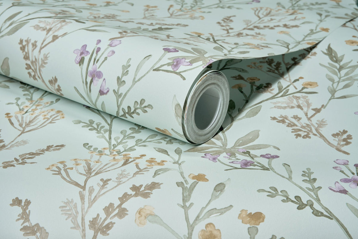 A partially unrolled roll of Chesapeake Laverne Wildflowers Wallpaper by York Wallcoverings, featuring a light blue background adorned with delicate floral patterns in shades of green, purple, and yellow, rests on a flat surface.