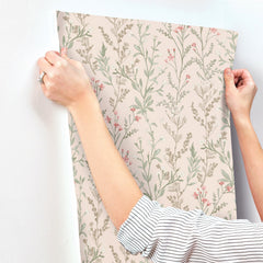 A person in a striped shirt is applying the Chesapeake Laverne Wildflowers Wallpaper by York Wallcoverings, which features pink and green botanical patterns, to a white wall.