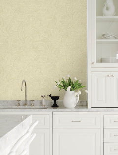 Modern white kitchen featuring marble countertops, a sink, and open shelves displaying plates. The walls are adorned with Chesapeake Harrison Swirling Geometric Wallpaper by York Wallcoverings in a light beige pattern. Beside the faucet sits a white pitcher with white tulips and a black decorative bird.