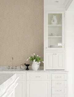 A bright white kitchen featuring marble countertops, a glass-front cabinet displaying dishes, and a white pitcher of tulips beside the faucet and a small black bird figurine, with the walls adorned in York Wallcoverings’ Chesapeake Harrison Swirling Geometric Wallpaper.