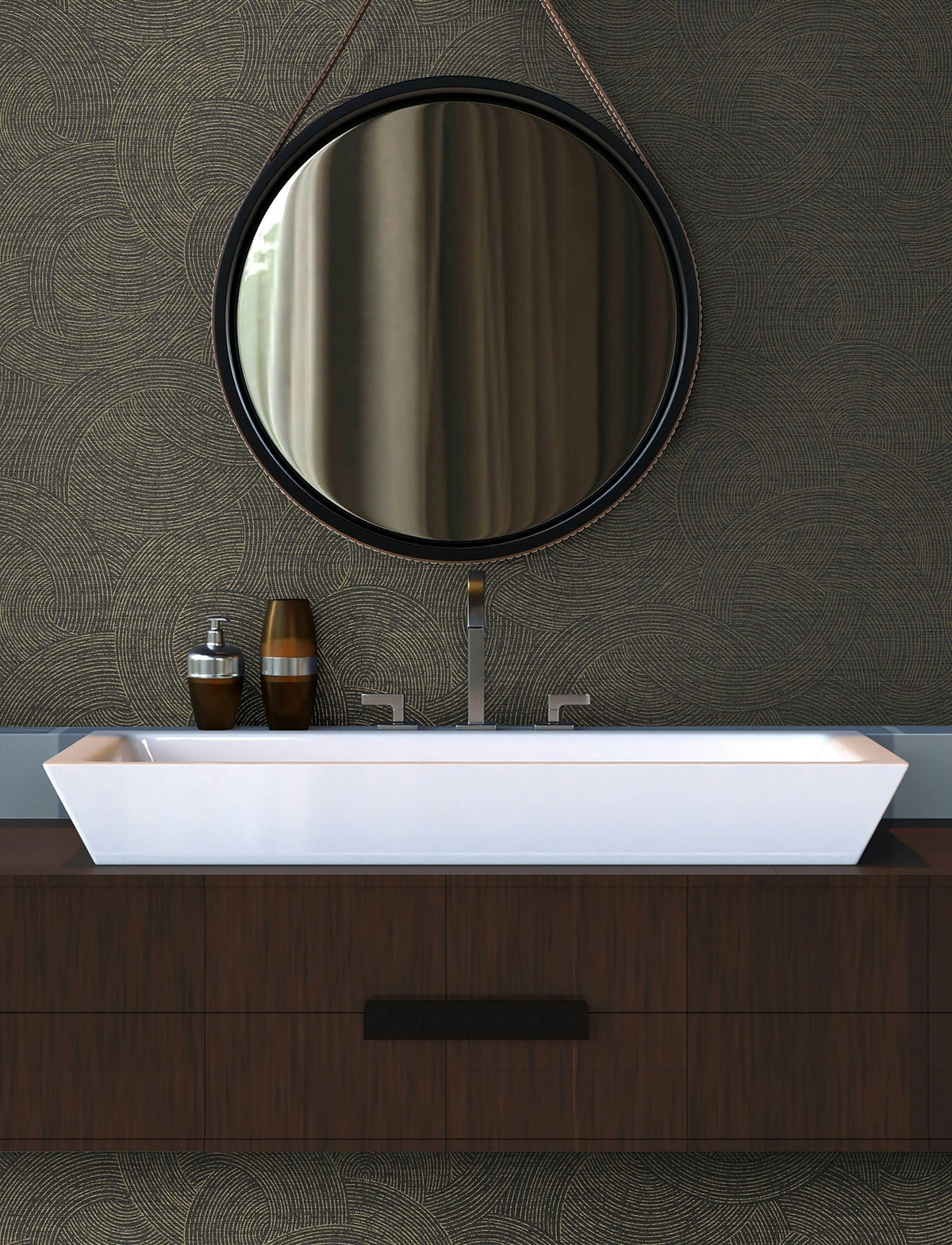 A modern bathroom featuring a round mirror, York Wallcoverings’ Chesapeake Harrison Swirling Geometric Wallpaper, a rectangular white sink, and dark wood cabinetry. Two decorative bottles are arranged on the counter beside the sink.