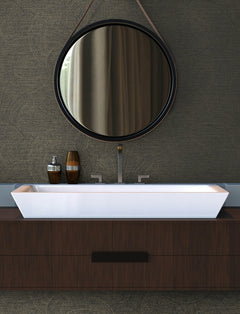 A modern bathroom featuring a round mirror, York Wallcoverings’ Chesapeake Harrison Swirling Geometric Wallpaper, a rectangular white sink, and dark wood cabinetry. Two decorative bottles are arranged on the counter beside the sink.