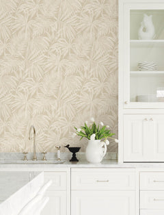 Bright kitchen with white cabinets, marble countertops, Chesapeake Sonny Fronds Wallpaper by York Wallcoverings in beige, a vase of white tulips, and a glass-front cabinet displaying plates and a decorative pitcher shaped like a bird.