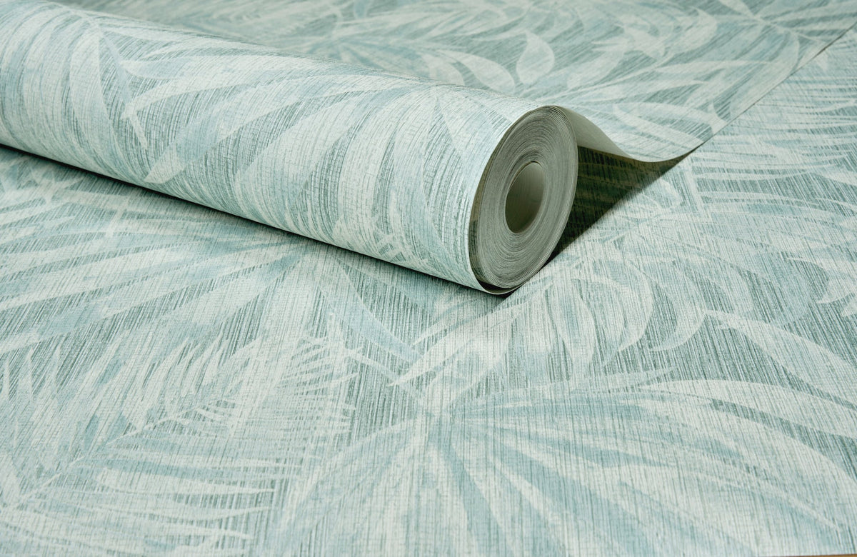 A close-up of a partially unrolled Chesapeake Sonny Fronds Wallpaper by York Wallcoverings, featuring a light green and white leafy pattern, displayed on a flat surface.