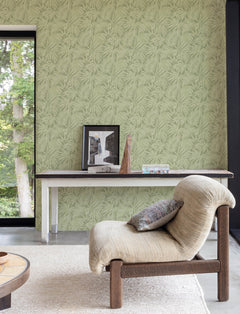 A modern living room featuring York Wallcoverings’ Chesapeake Sonny Fronds Wallpaper, a light cushioned chair, a white console table adorned with decor, and a large window revealing lush green trees outside.