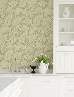 A white kitchen with marble countertops, a sink, a cabinet with glass doors, white dishes, a vase of white tulips, and York Wallcoverings’ Chesapeake Sonny Fronds Wallpaper in beige palm leaf pattern on the wall.