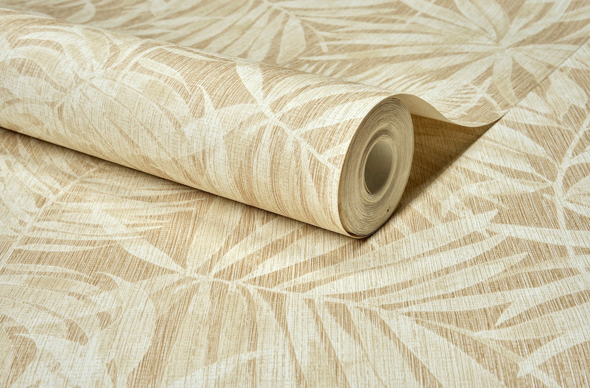 A roll of Chesapeake Sonny Fronds Wallpaper by York Wallcoverings, showcasing a beige and cream leafy pattern with tropical palm leaf designs, lies partially unrolled on a flat surface.
