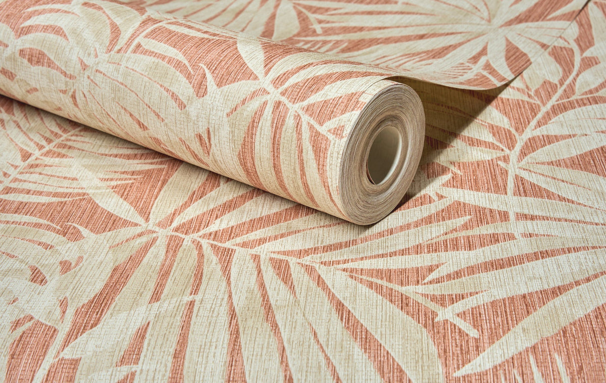 A partially unrolled roll of Chesapeake Sonny Fronds Wallpaper by York Wallcoverings, featuring a beige and rust-colored tropical leaf pattern, displayed on a flat surface.