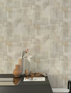 A minimalist table with neutral-toned ceramics, a single branch with white flowers, and papers sits in front of a wall adorned with Chesapeake Cassandra Block Geometric Wallpaper by York Wallcoverings.