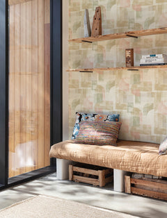 A cozy corner featuring a tan cushioned bench with colorful throw pillows, wooden crates for storage underneath, and wooden shelves displaying books and decor, is nestled beside a large window framed with wooden paneling. The walls are adorned with Chesapeake Cassandra Block Geometric Wallpaper by York Wallcoverings, adding a modern touch to the space.