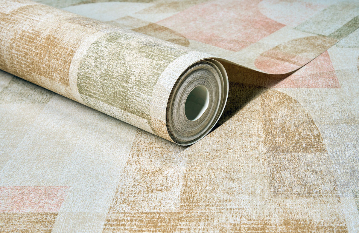 A partially unrolled roll of Chesapeake Cassandra Block Geometric Wallpaper by York Wallcoverings, featuring a muted geometric pattern in beige, light green, and soft pink tones on a matching surface.