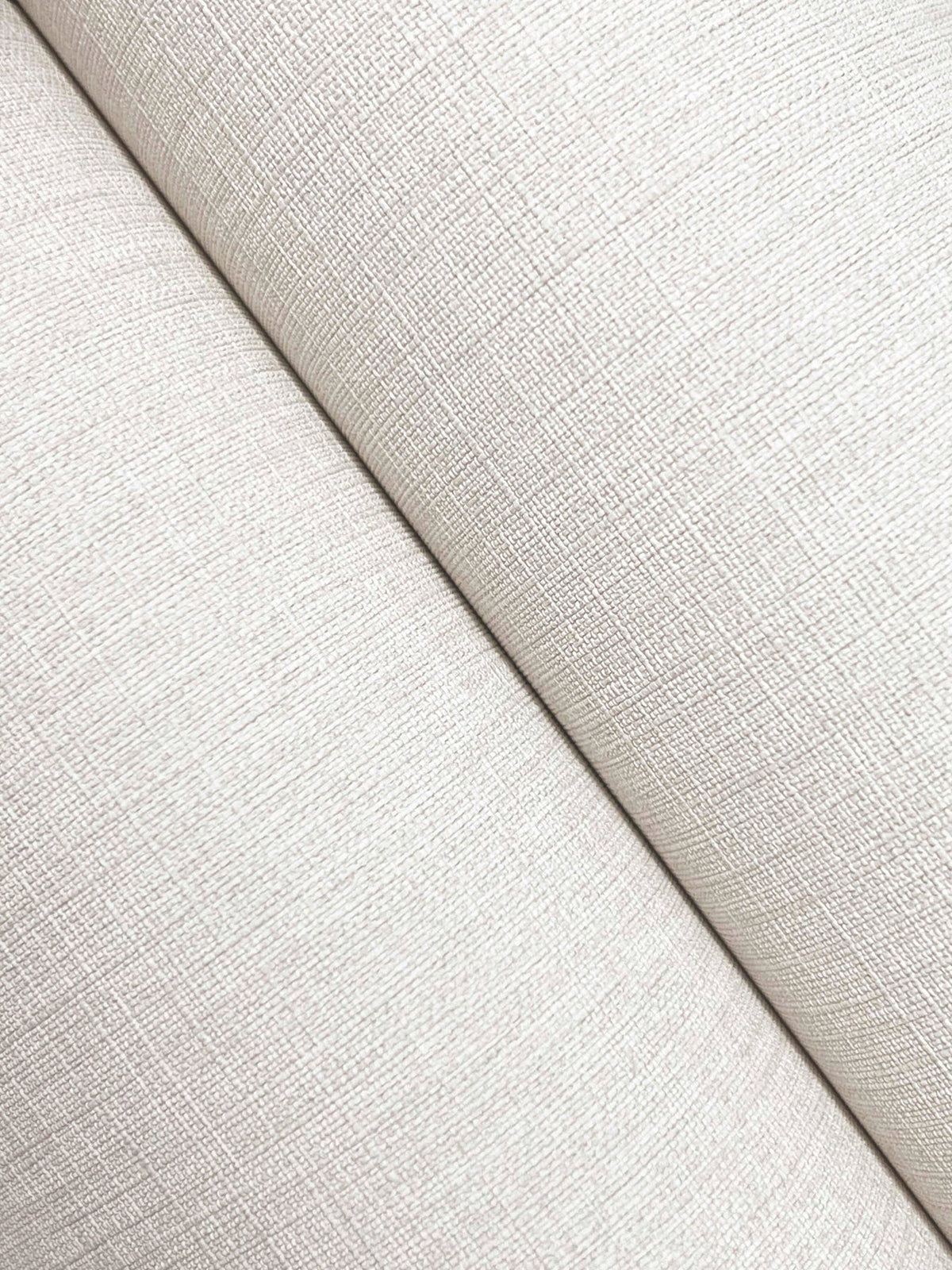 Close-up of two cream-colored Chesapeake Sonia Faux Linen Wallpaper surfaces by York Wallcoverings intersecting diagonally, highlighting a fine crosshatch pattern and soft lighting.