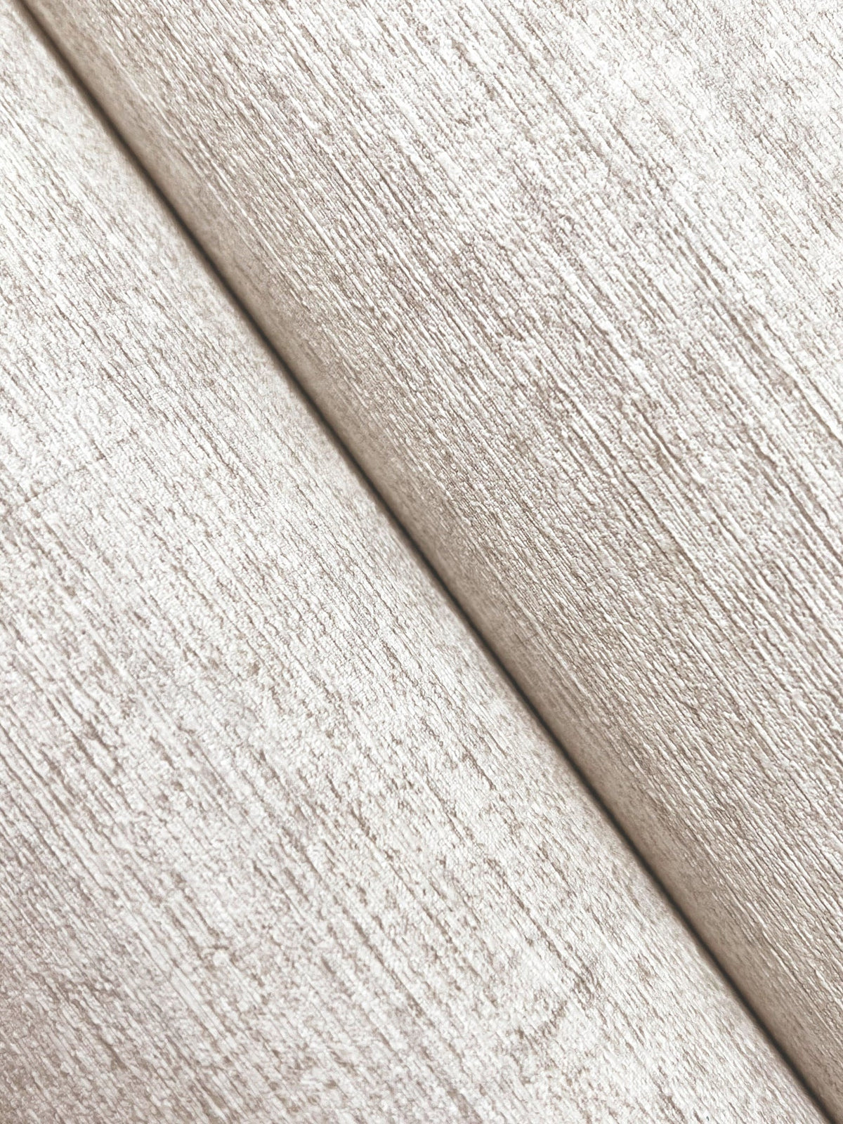 Close-up of two pieces of Chesapeake Tansy Distressed Wallpaper by York Wallcoverings overlapping diagonally, showcasing a subtle horizontal and vertical grain pattern on the textured beige surface.