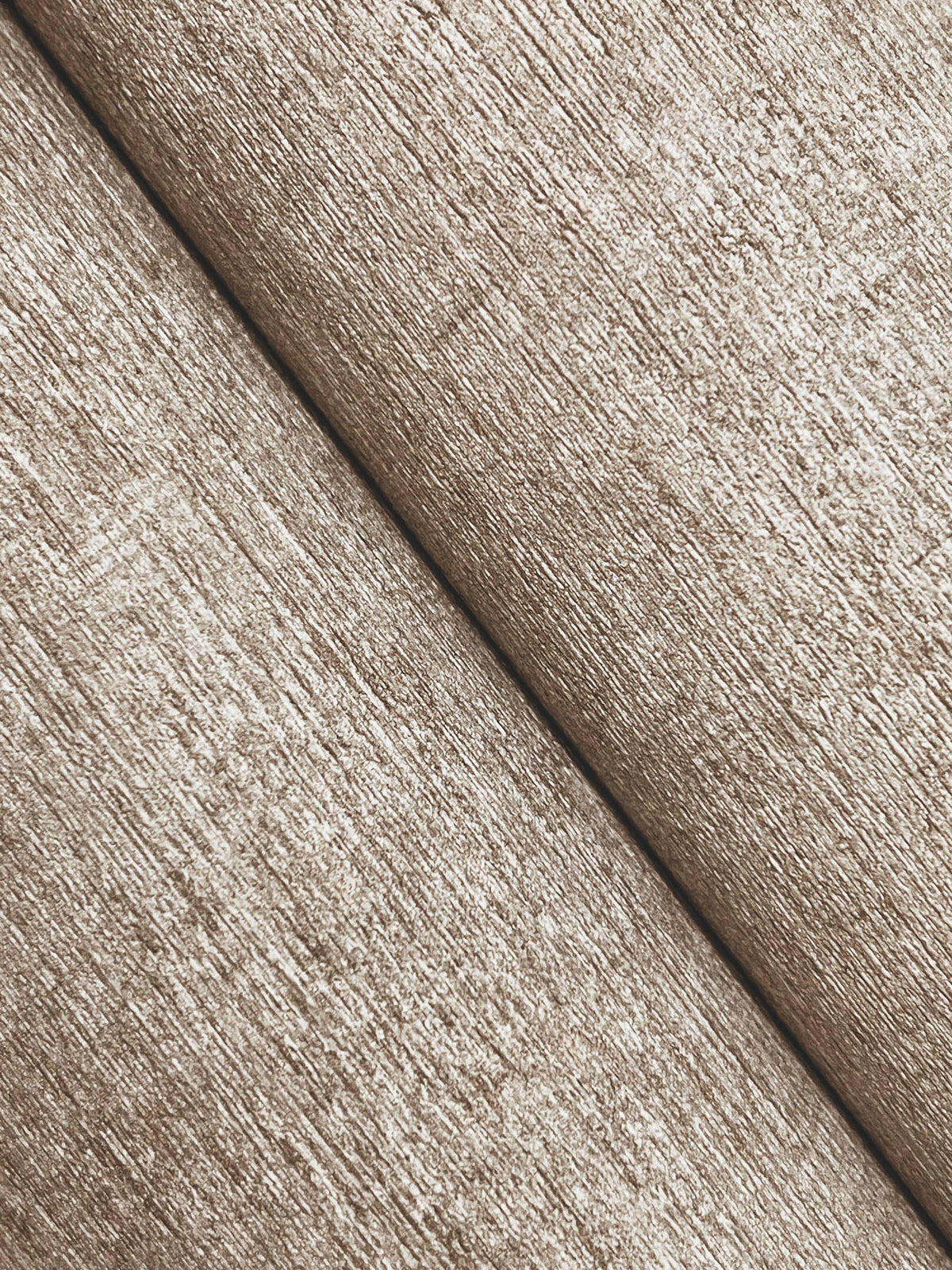 Close-up of Chesapeake Tansy Distressed Wallpaper by York Wallcoverings, featuring a textured, beige surface with two diagonal folds that create subtle shadows and depth. The wallpaper appears soft with a slightly rough finish.